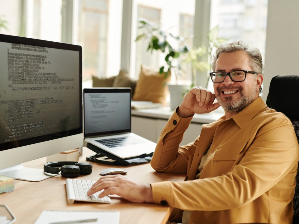 Successful mature IT engineer looking at camera by workplace